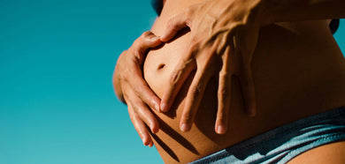 belly of a pregnant woman with her hands on it in a clear sky background