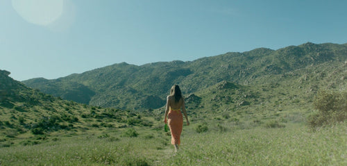 Woman dressed in yellow walking in a green field in a sunny day