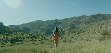 Woman dressed in yellow walking in a green field in a sunny day
