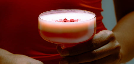 close up of orange in martini glass held by a woman wearing an orange blouse
