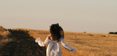 Person with long hair standing in a field at sunset